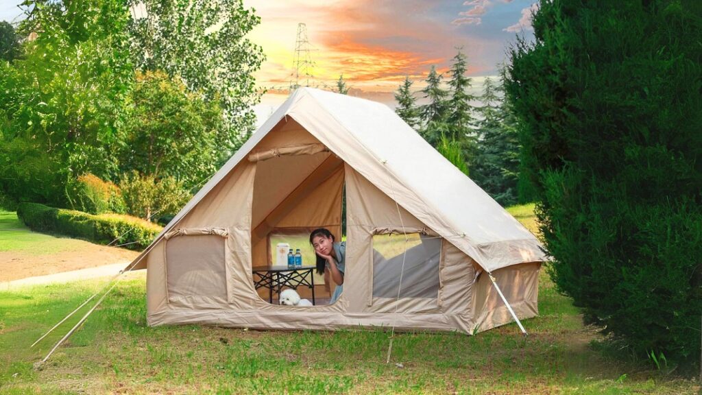 An inflatable cabin tent that is set up in a beautiful garden with a sunset view in the background.